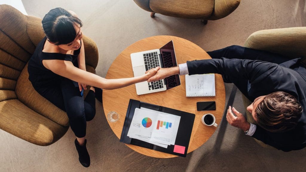 Two business professionals shaking hands over an app development outsourcing agreement.