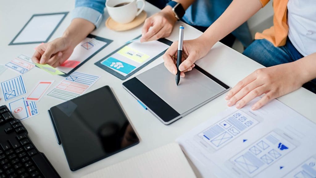 A team designing a mobile app UI/UX on a digital tablet.